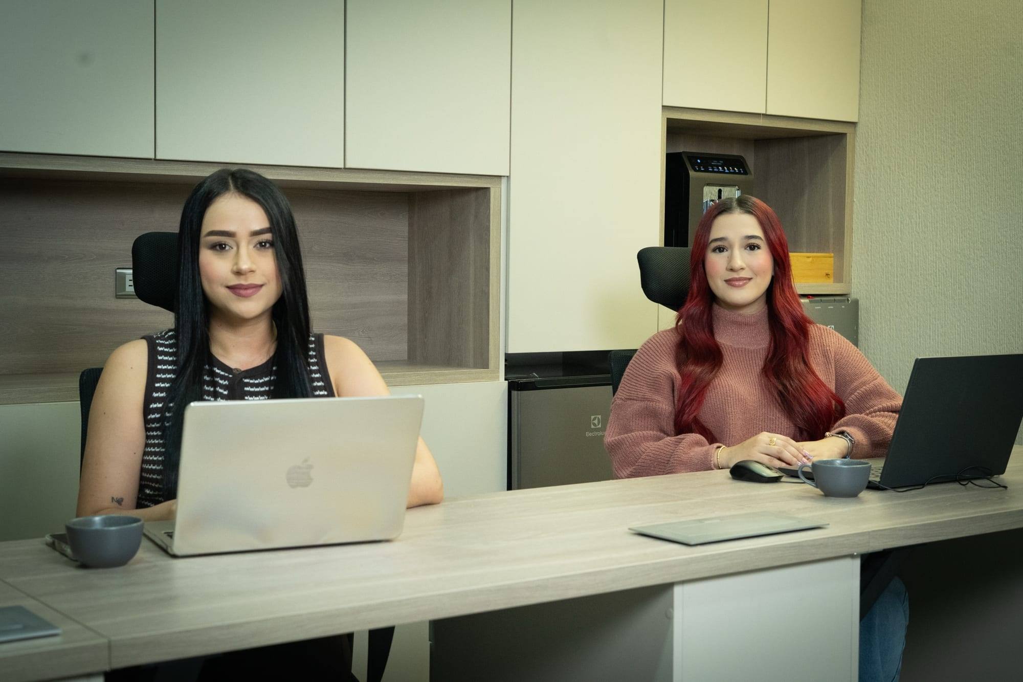 Dos integrantes del equipo en sus puestos de trabajo, mirando a cámara