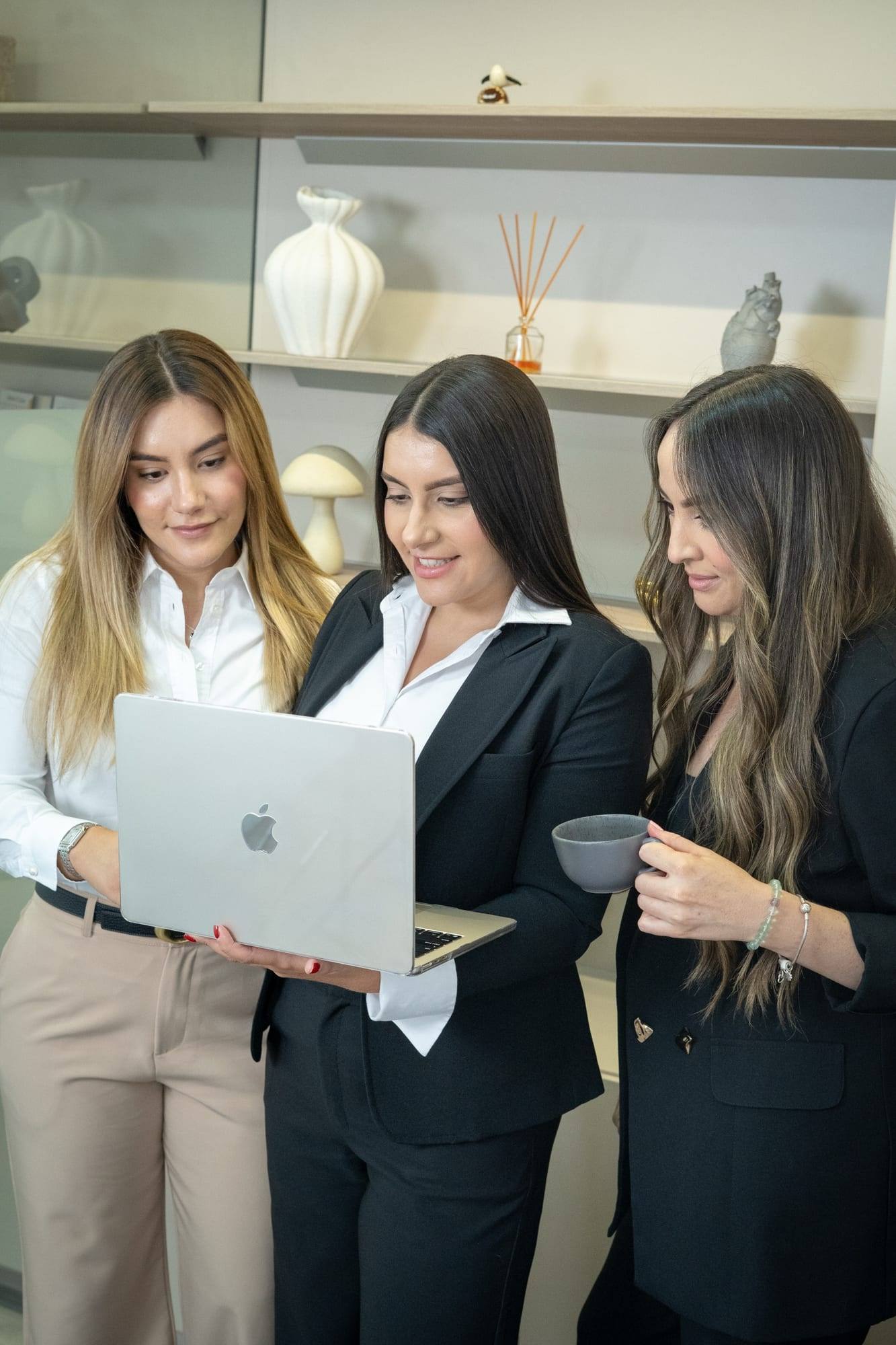 Tres integrantes de Solvé Abogados de pie; una sostiene un portátil abierto, en una oficina con estantería